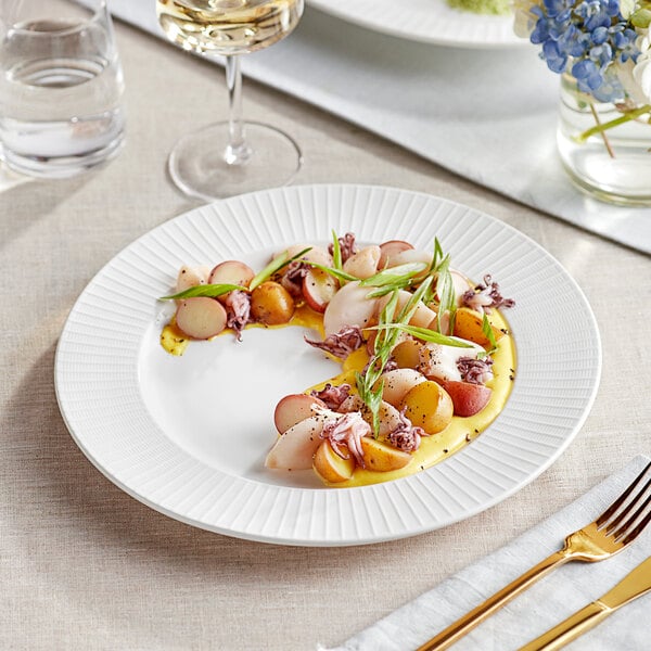 An Acopa Cordelia white porcelain plate with food on a table next to a glass of white wine.