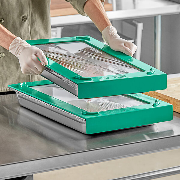 A gloved hand using plastic wrap to cover a stainless steel hotel pan on a table.