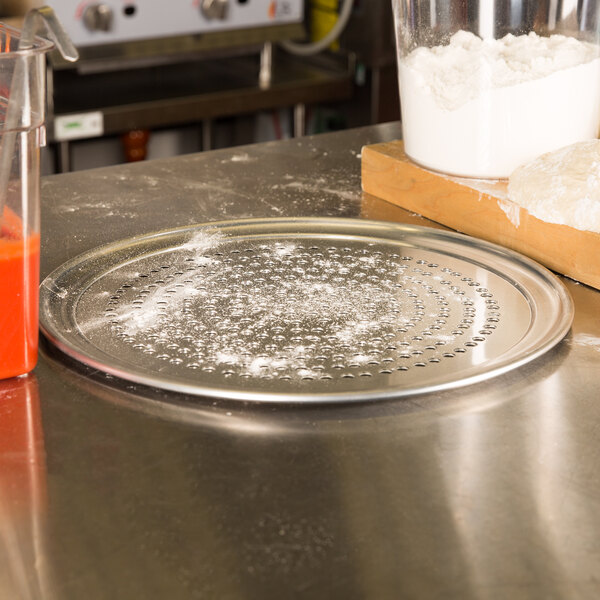 An American Metalcraft Super Perforated Heavy Weight Aluminum Pizza Pan with flour on it next to a bowl of flour and a blender.