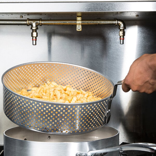 A hand holding a Vollrath metal basket with food over a Vollrath fryer pot