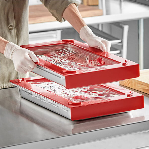 A gloved hand uses a red Pan Stackers container to wrap a tray of food.