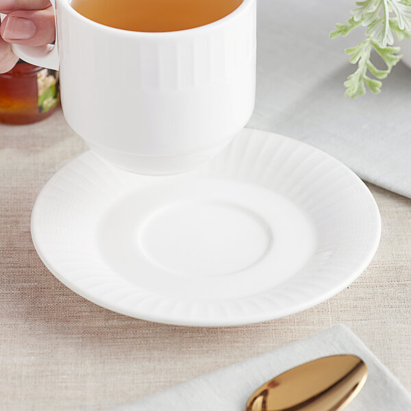 A hand holding a white mug of tea on a white Acopa Cordelia saucer.