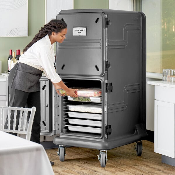 A woman putting food into a Cambro Pro Cart Ultra food container.