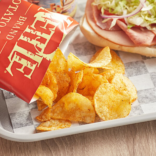 A bag of Kettle Brand Backyard Barbeque potato chips and a sandwich on a table.