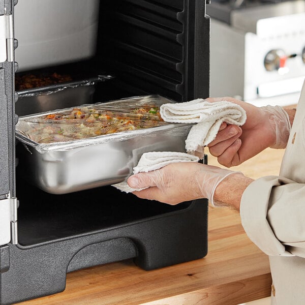 A person using a Vollrath stainless steel steam table pan to cook food in an oven.