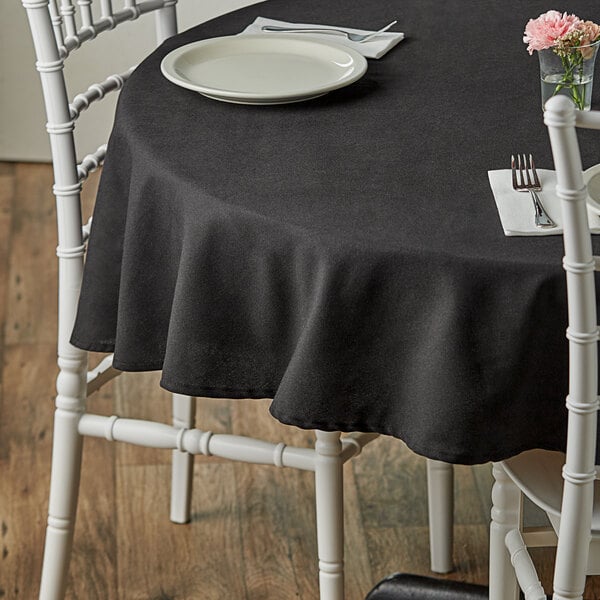 A table with a black Choice 100% Spun Polyester Hemmed Cloth Table Cover and a white chair.