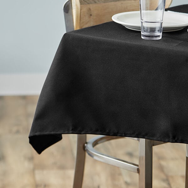 A black Choice square table cover on a table with a plate and glass.