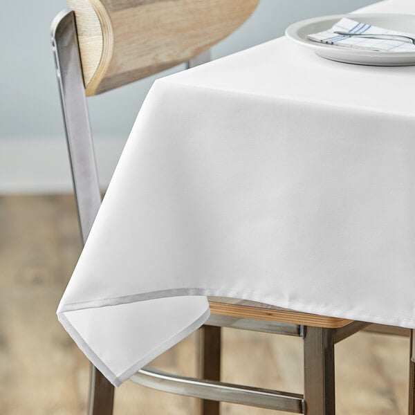 A table with a white Choice square table cover and a plate with a fork on it.