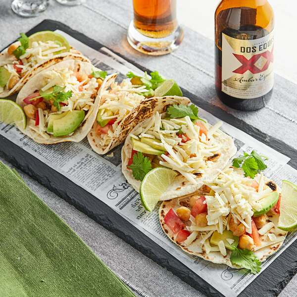 A stone tray with three tacos filled with vegetables and Daiya Vegan Jalapeno Havarti cheese.