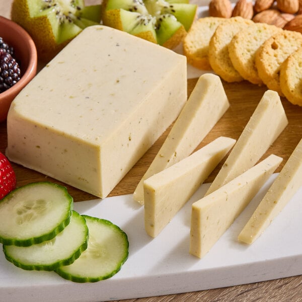 A cutting board with a block of Daiya Vegan Jalapeno Havarti cheese, crackers, and fruit.