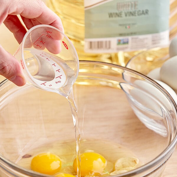 A hand pouring Colavita White Wine Vinegar into a bowl of eggs.