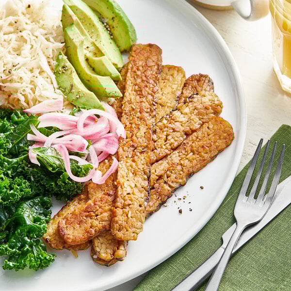 A plate of food with Lightlife Smoky Tempeh Strips, vegetables, and a fork.