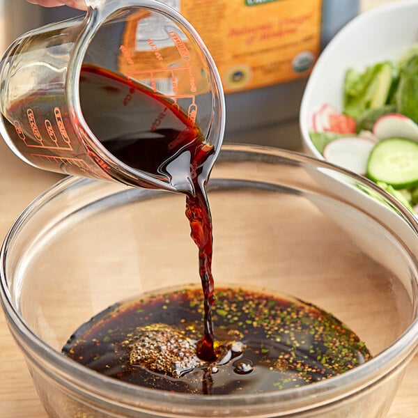 A person pouring Colavita Organic Balsamic Vinegar into a bowl of food.