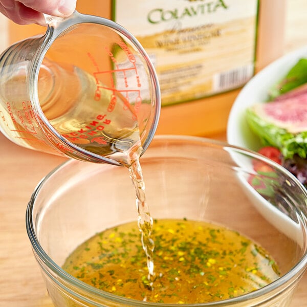 A person pouring Colavita Prosecco wine vinegar into a glass bowl of salad.