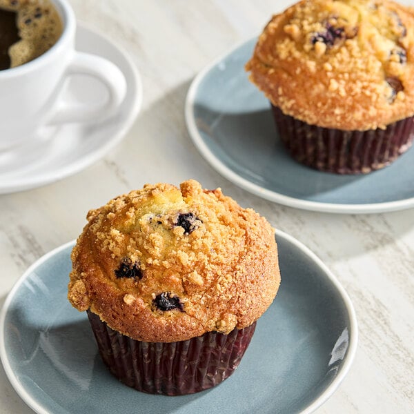 Two David's Cookies blueberry muffins on plates next to a cup of coffee.