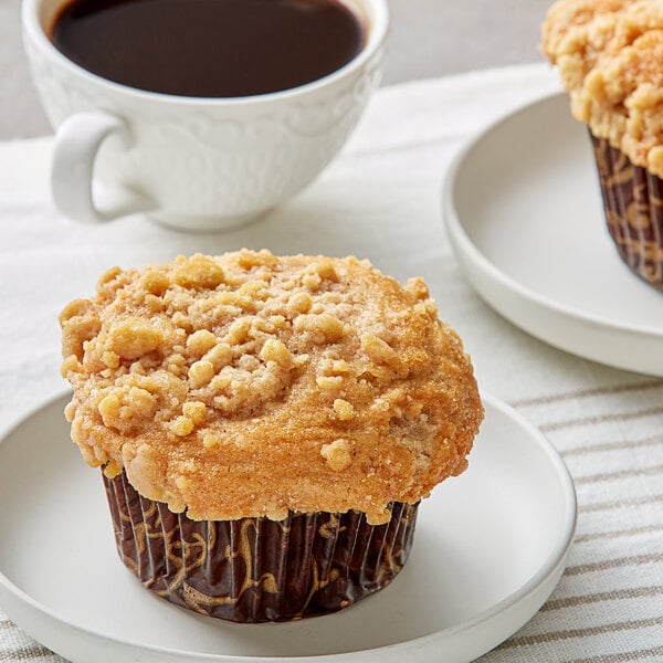 A David's Cookies apple streusel muffin on a white plate with a cup of coffee.