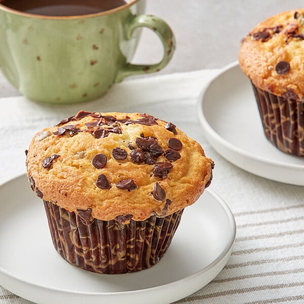 Two David's Cookies chocolate chip muffins on white plates next to a mug of coffee.