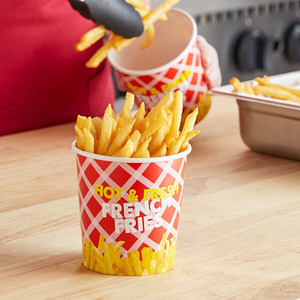 A person in a red apron putting French fries into a Choice paper cup.