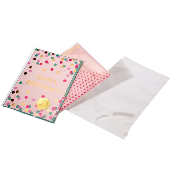 A white envelope with a pink polka dot design containing a pink card with gold text and polka dots.