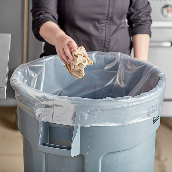 A hand holding a crumpled paper throws it into a clear poly bag.