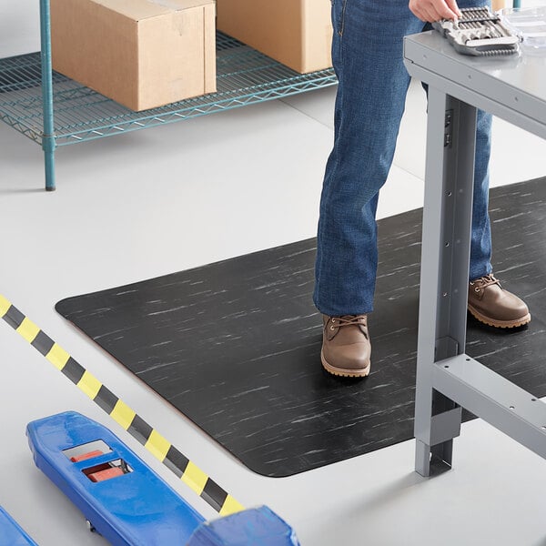 A person standing on a black and white Lavex K-Marble Foot anti-fatigue mat.