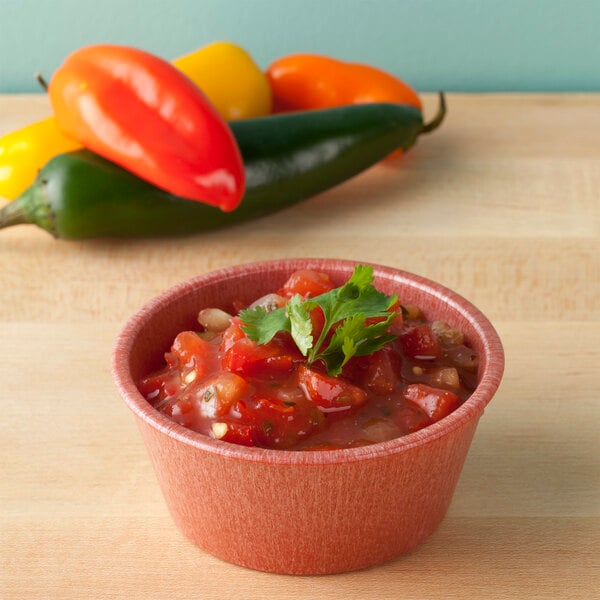 A bowl of salsa on a table with a leafy green garnish.