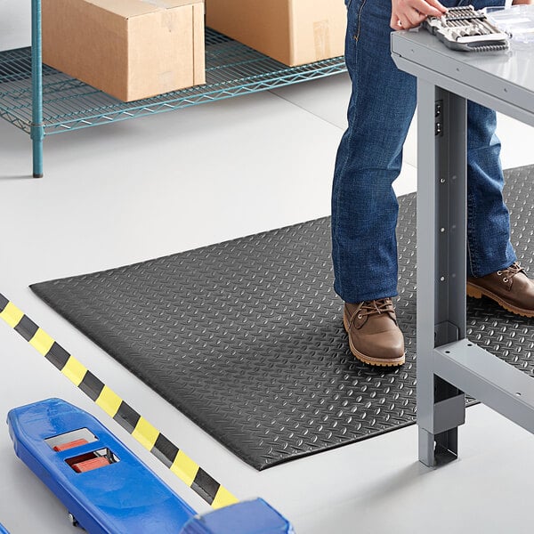 A black 2-foot by 60-foot anti-fatigue mat with a diamond plate texture, designed for use in workspaces.