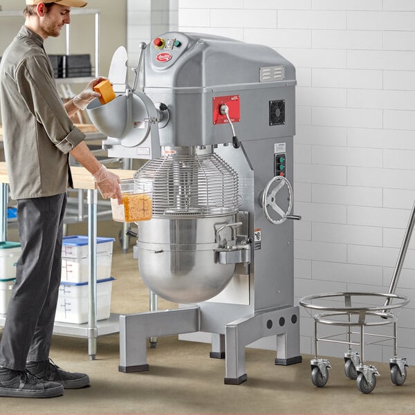 A man standing next to an Avantco 60 quart floor mixer with shredder attachment and guard.