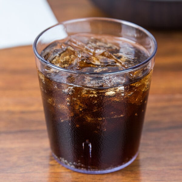 A Cambro clear plastic tumbler filled with ice tea on a table with ice and brown liquid.