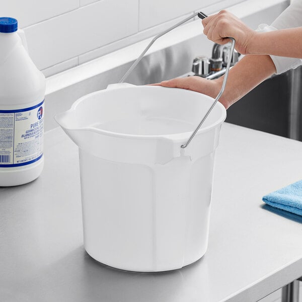 A person washing a Lavex white round bucket on a counter.