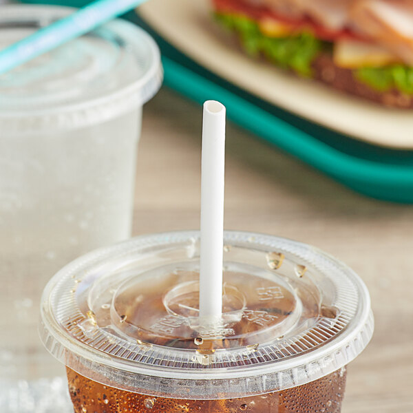 A plastic cup with a SOFi white paper straw in it on a table with a sandwich.