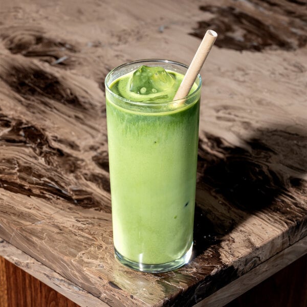 A tall glass of iced green matcha latte with a large kraft paper straw on a marbled table.
