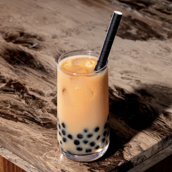A glass of iced bubble tea with black tapioca pearls and a black paper boba straw.