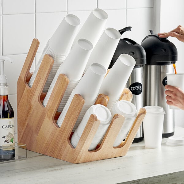 A wooden holder with white cups and a slanted cup dispenser.