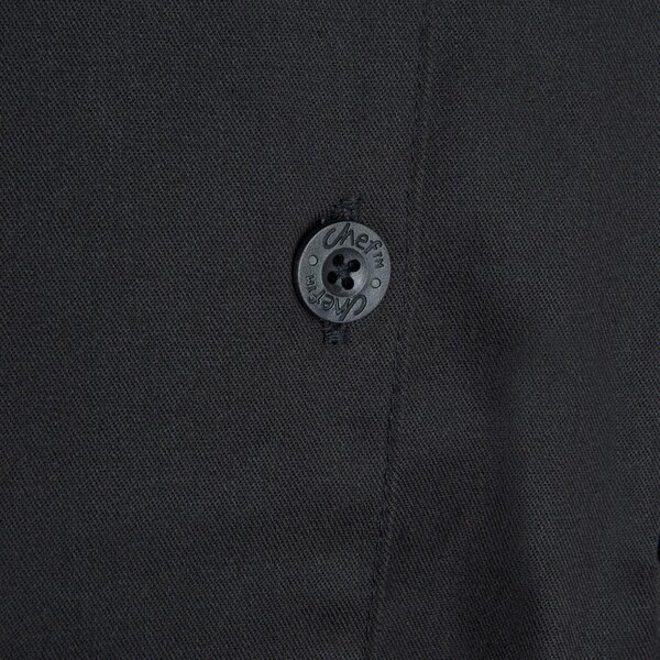 A close up of a black button on a black Chef Revival chef coat.