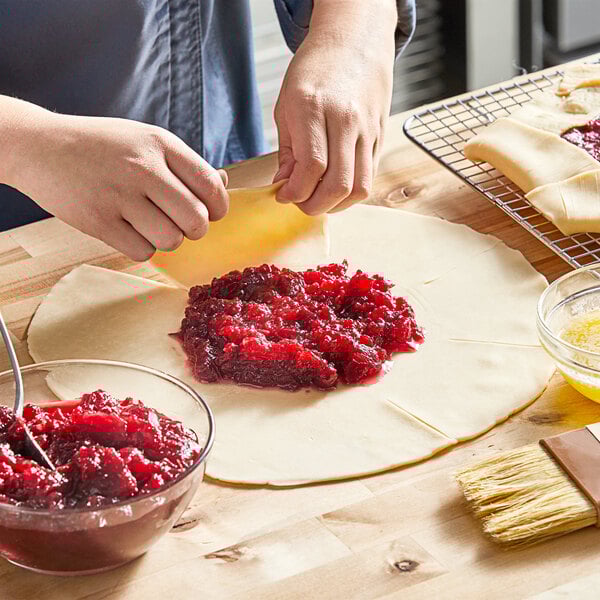 A person making a cranberry pie with a bowl of Ocean Spray Whole Berry Cranberry Sauce.