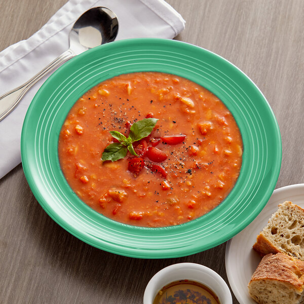 A Tuxton Cilantro china bowl of soup with a spoon and a plate of bread.