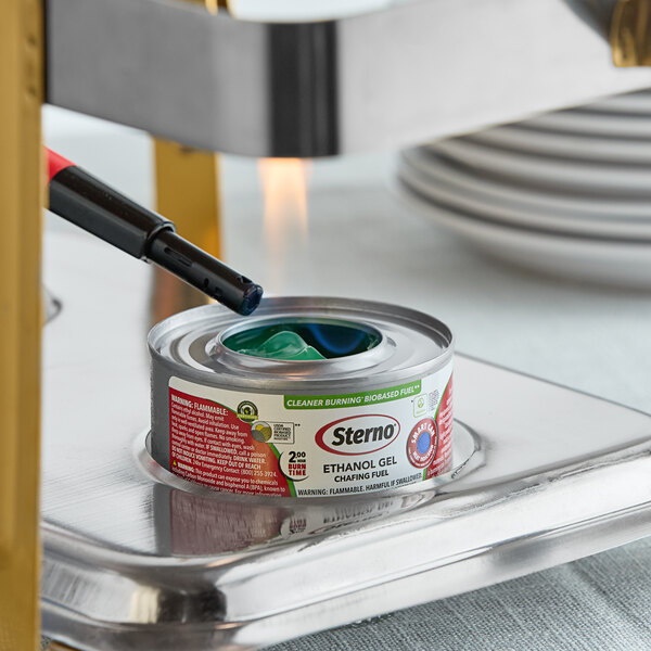 A can of Sterno ethanol gel chafing fuel being lit with a lighter under a chafing dish.