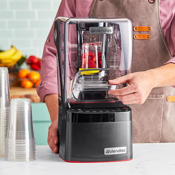 A person using a Blendtec Stealth Nitro X blender with a black and red sound enclosure.