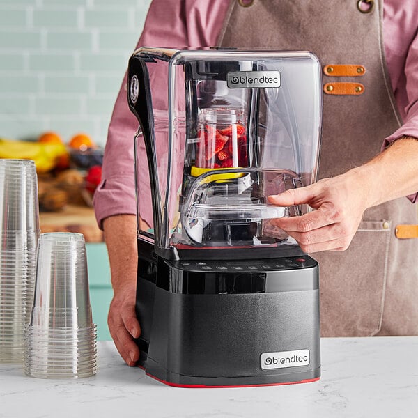 A man using a Blendtec Stealth Nitro X blender on a counter in a smoothie shop.