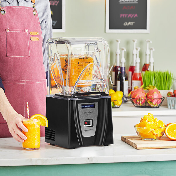 A man in an apron using a Blendtec Connoisseur 825 blender to make a yellow drink.