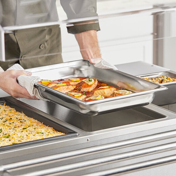 A person holding a Vollrath stainless steel steam table tray of food.