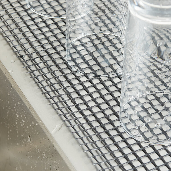 Clear glasses sitting on a metal mesh shelf lined with black plastic mesh.