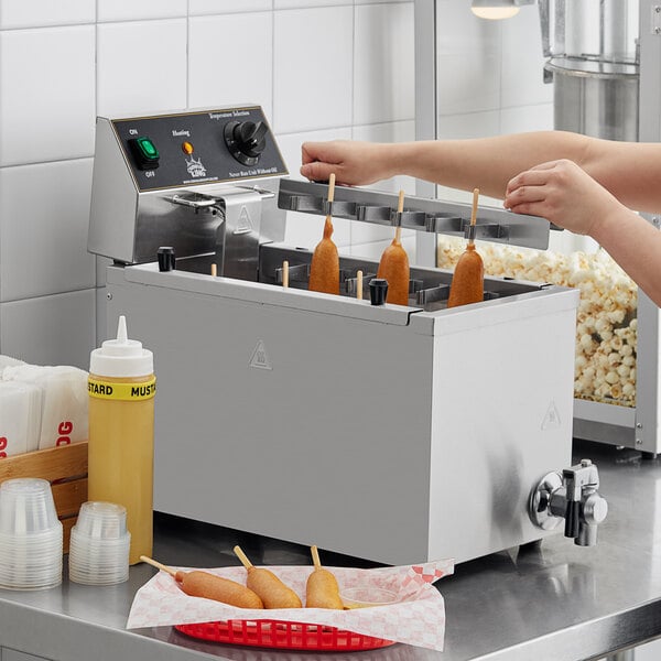 A woman using a Carnival King corn dog fryer to cook corn dogs on a counter.