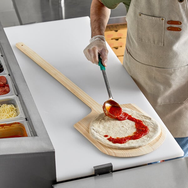 A man using a Choice wooden pizza peel to spread sauce on a pizza.