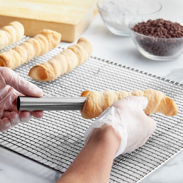 A person's hand holding an Ateco stainless steel cream roll form.