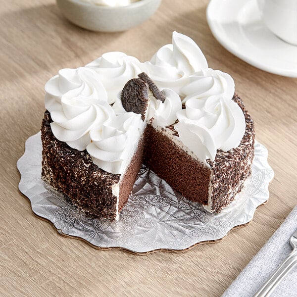 A piece of cake on a silver Enjay laminated cake circle with white frosting and a cookie on top.