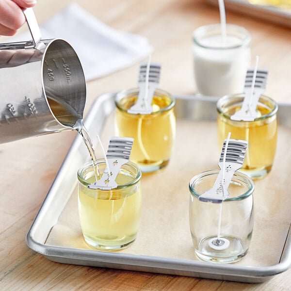 A person pouring white liquid into Acopa glass votive jars on a tray.