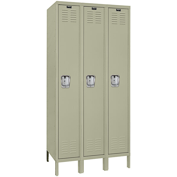 A beige metal Hallowell triple locker with recessed handles and three doors.