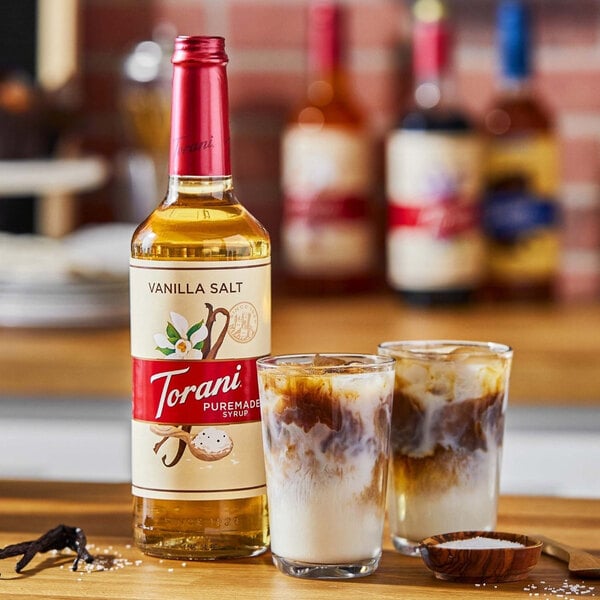 A bottle of Torani Vanilla Salt flavoring syrup next to a glass of vanilla flavored drink.